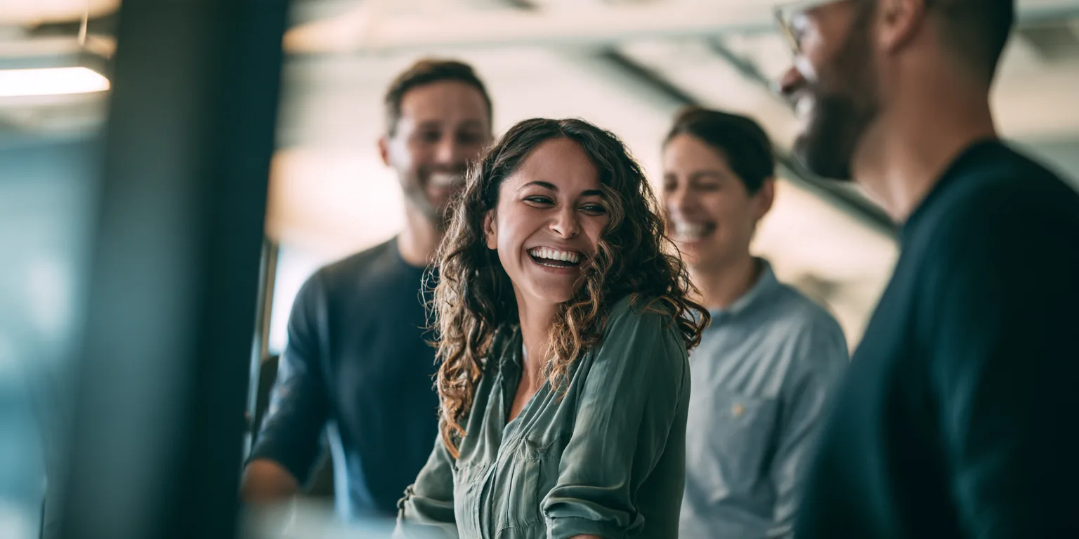 A small team of three colleagues in their 20s to 40s gathered around a standing desk in a bright modern office